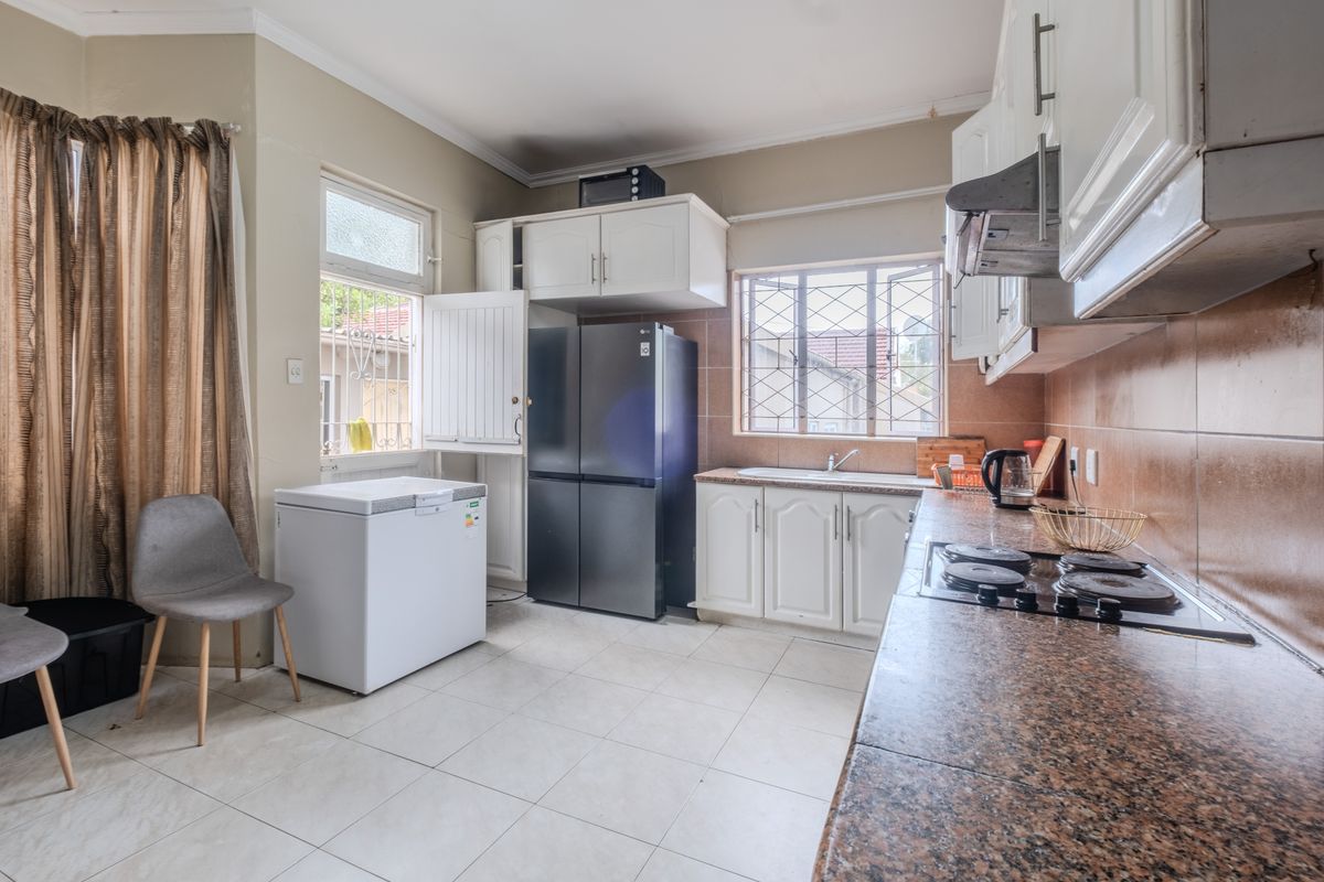 Functional kitchen featuring granite countertops, built-in cabinetry, electric hob, extractor fan, and tiled flooring with security bars on the windows.