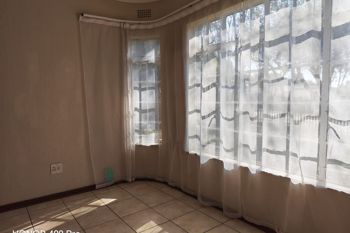 A bright living area featuring large bay windows with natural light, tiled flooring, and neutral wall finishes.
