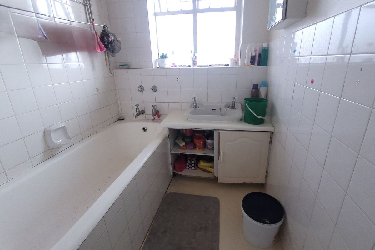 A dated bathroom featuring a standard bathtub, a single basin with a vanity cabinet, and white wall tiling throughout.