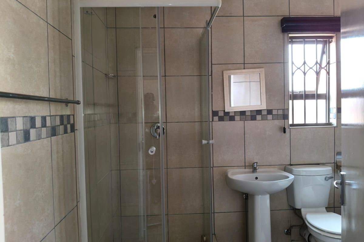 A functional bathroom featuring a glass shower enclosure, pedestal basin, toilet, and neutral wall tiling with decorative accents.