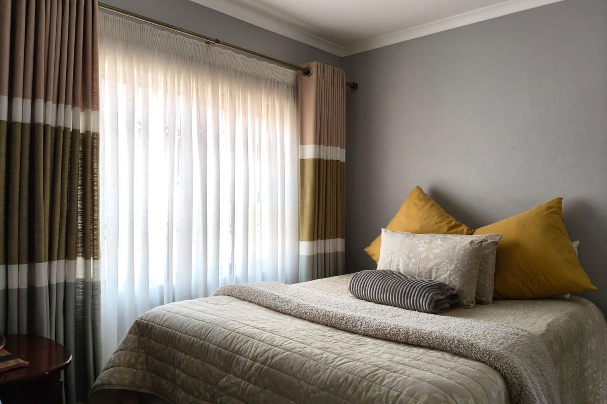 A cozy bedroom featuring neutral grey walls, a large window with layered curtains, and decorative cove cornicing.