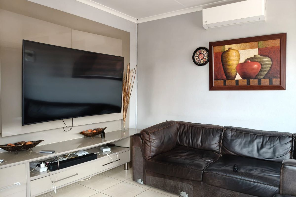 A living room featuring a built-in media console, tiled flooring, and a wall-mounted air conditioning unit.