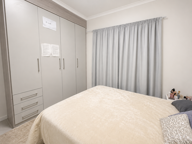 A well-maintained bedroom featuring a large, modern built-in wardrobe with integrated drawers and neutral finishes.