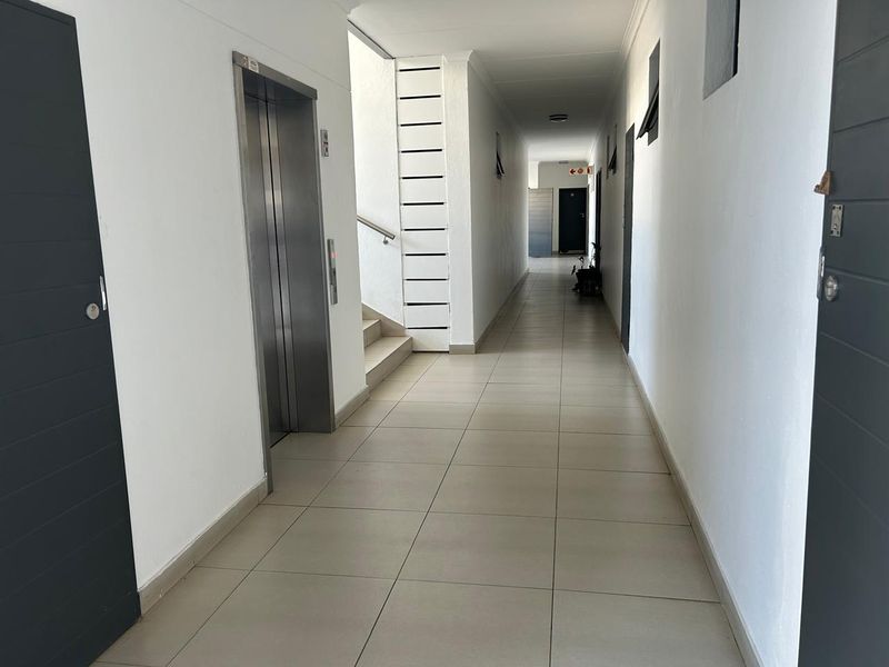 A clean, well-maintained apartment building hallway featuring tiled flooring, a modern elevator, and access to a staircase.