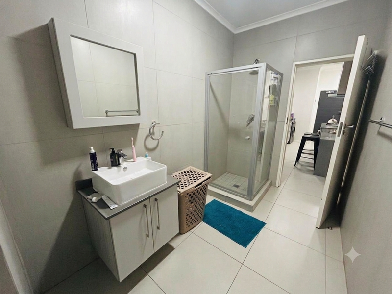 A modern bathroom featuring a vessel sink vanity, wall-mounted mirror, and a glass-enclosed shower with neutral floor-to-ceiling tiling.