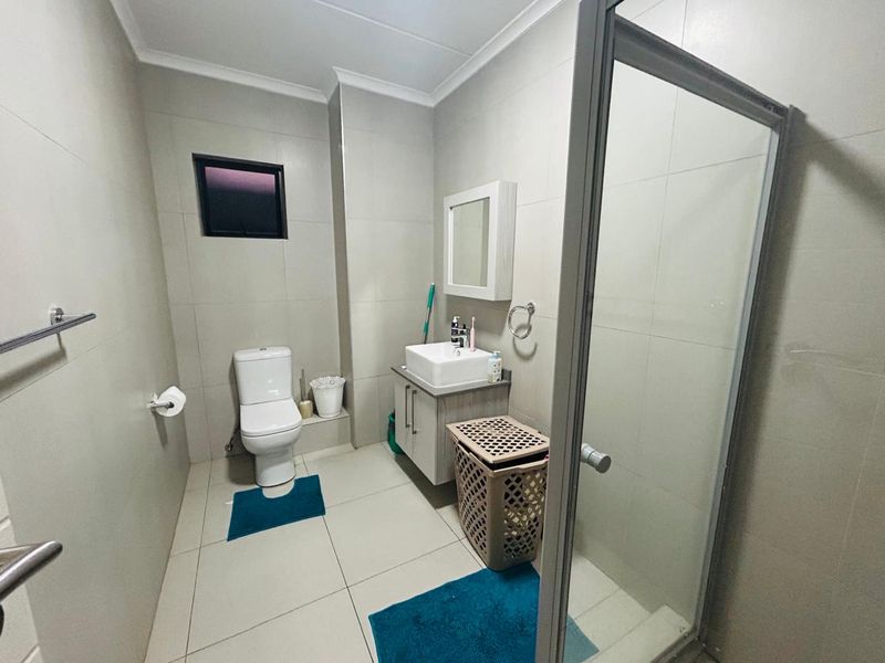 A functional bathroom featuring a shower enclosure, vanity cabinet with basin, toilet, and neutral wall and floor tiling.