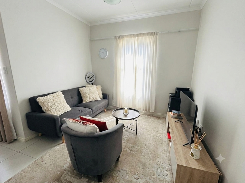 A bright and comfortable living room featuring neutral tiled flooring and a large window with installed curtain rails.