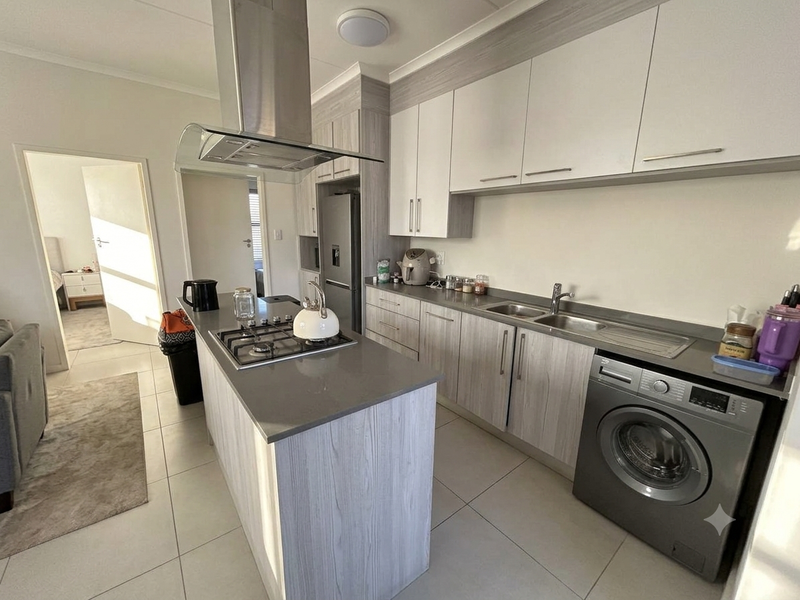 Modern kitchen featuring light wood-grain cabinetry, stone countertops, a gas hob with extractor, and a built-in washing machine, finished with neutral floor tiles.