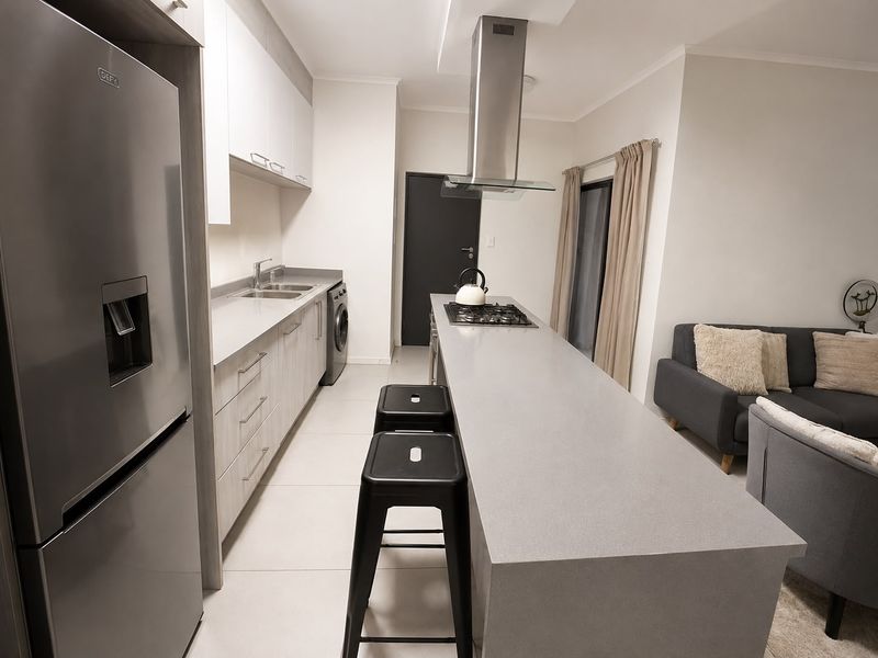 Modern open-plan kitchen featuring sleek cabinetry, stone countertops, a gas hob with extractor fan, and integrated laundry space, flowing into the living area.