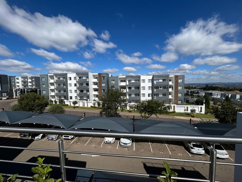 Elevated view overlooking the apartment complex, featuring a modern stainless steel balustrade and a paved parking area with shade cloth carports.