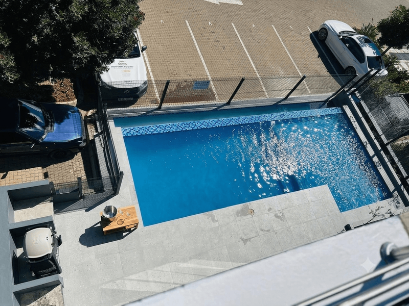 An elevated view of a private swimming pool area featuring a tiled deck, built-in braai, and secure perimeter fencing.