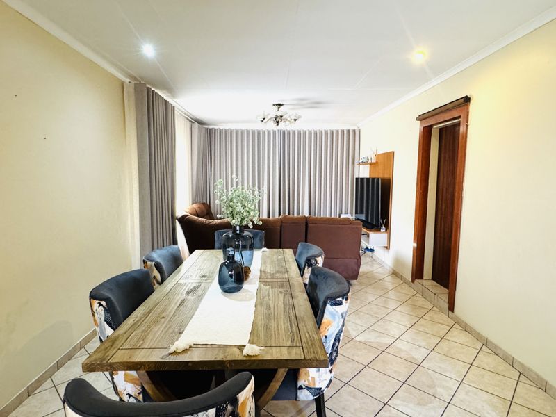 An open-plan living and dining area featuring tiled flooring, recessed lighting, and a central chandelier, creating a functional and connected living space.