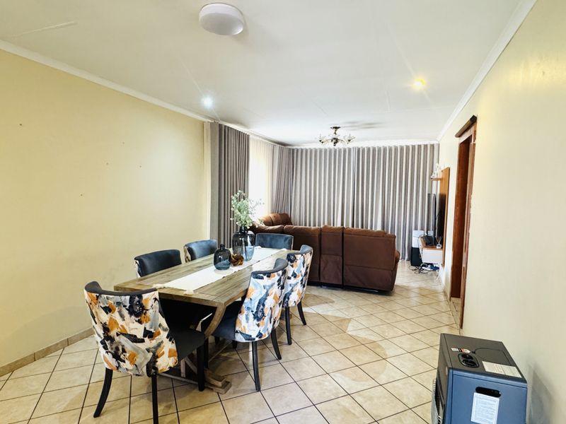 Spacious open-plan living and dining area featuring ceramic tile flooring, neutral wall tones, and full-length window treatments.