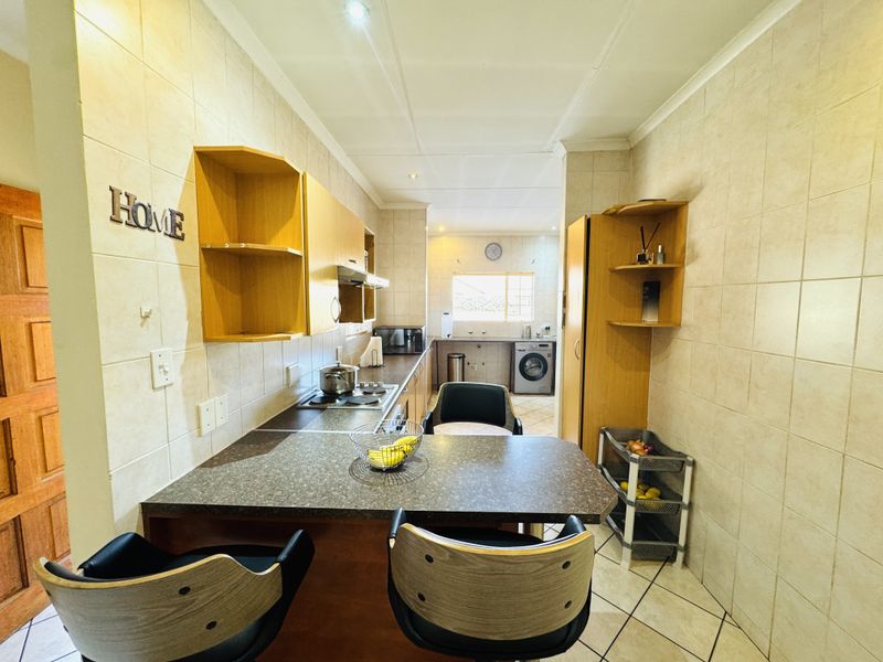A functional kitchen featuring laminate countertops, built-in cabinetry, and tiled finishes, with an integrated hob and extractor fan, leading into a separate laundry area.
