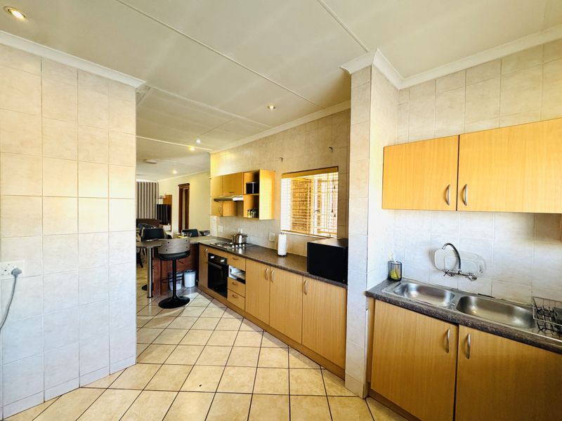 Functional kitchen featuring light wood cabinetry, laminate countertops, double stainless steel sink, built-in oven, and hob, with tiled flooring and splashbacks throughout.