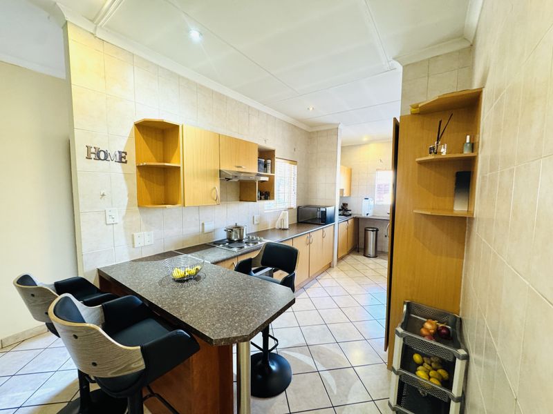 A functional kitchen featuring built-in wooden cabinetry, laminate countertops, a breakfast nook, and tiled finishes throughout.