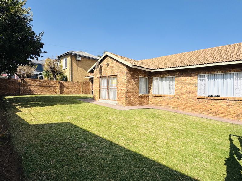 A well-maintained rear exterior view of a face brick house featuring a spacious lawn, paved walkway, and secure perimeter walling.