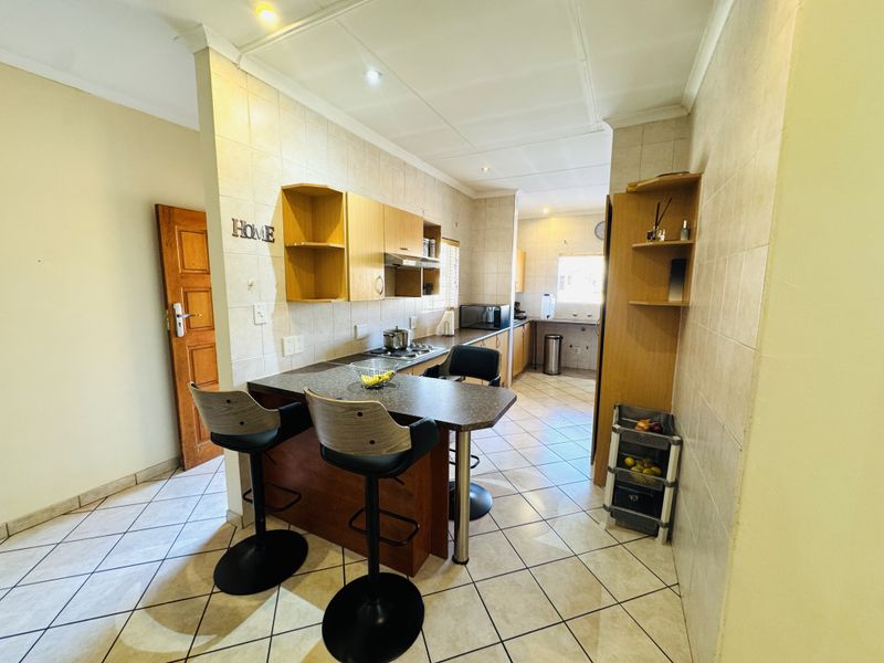 A functional kitchen featuring tiled flooring, built-in wooden cabinetry, a breakfast bar, and a tiled backsplash with integrated cooking appliances.