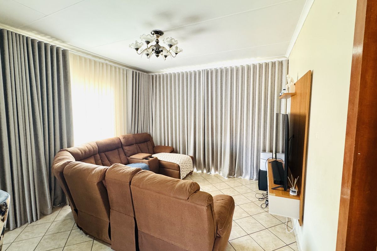 A living room featuring ceramic floor tiles, a wall-mounted media unit, and floor-to-ceiling curtains.