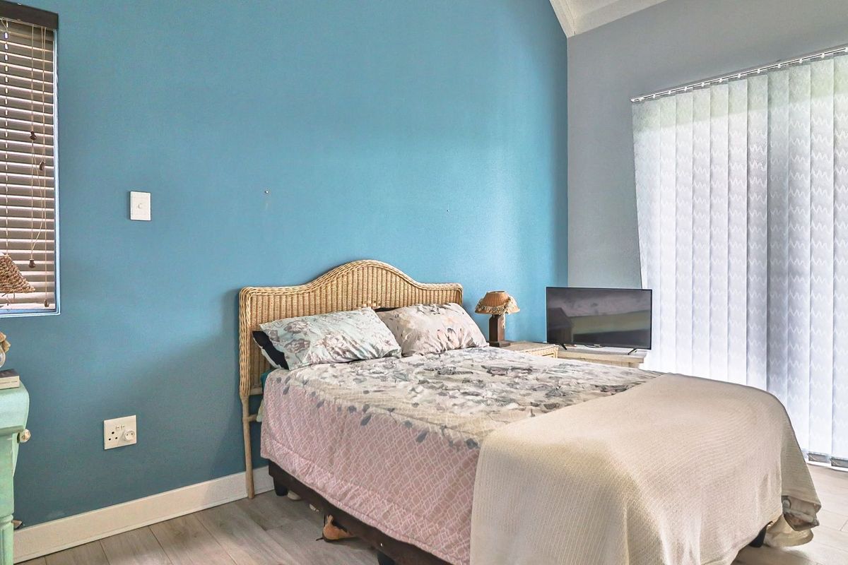 A bedroom featuring light-toned laminate flooring, a blue accent wall, and sliding glass doors with vertical blinds providing natural light.