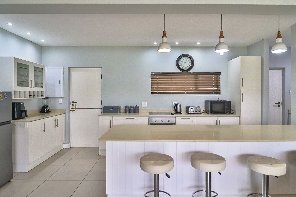 A bright, open-plan kitchen featuring white cabinetry, stone-look countertops, a central breakfast island, and integrated lighting, creating a clean and functional culinary space.