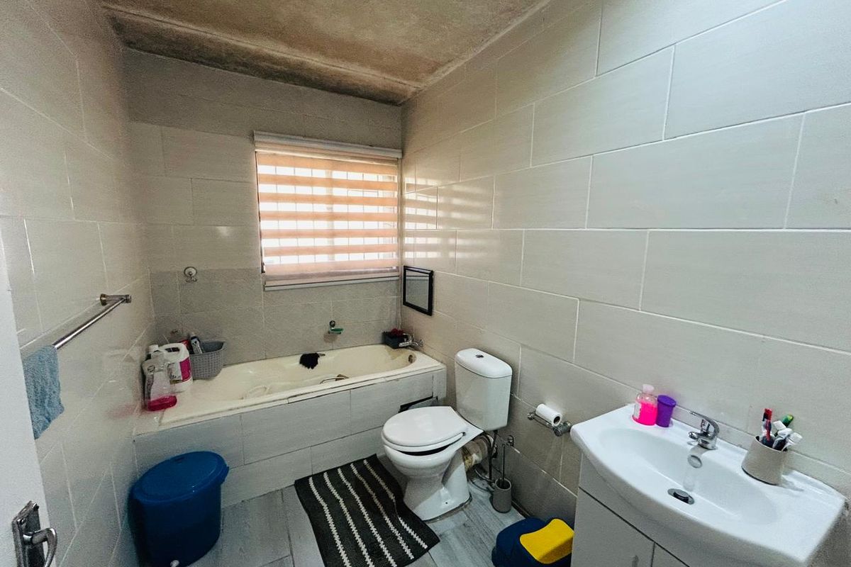 A functional bathroom featuring a built-in bathtub, a standard toilet, and a vanity basin with tiled walls and flooring.