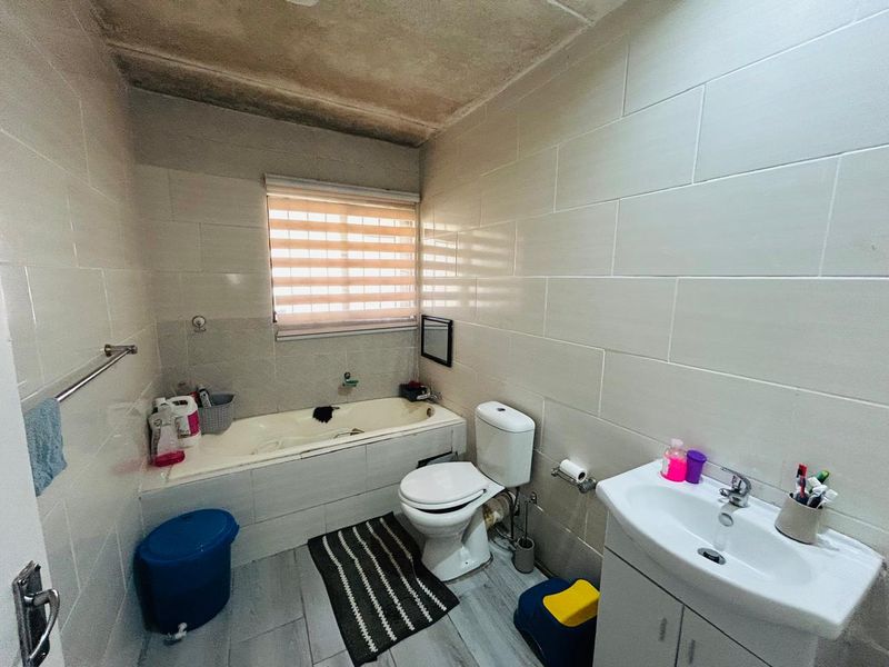 A functional bathroom featuring a built-in bathtub, a standard toilet, and a vanity basin with tiled walls and flooring.