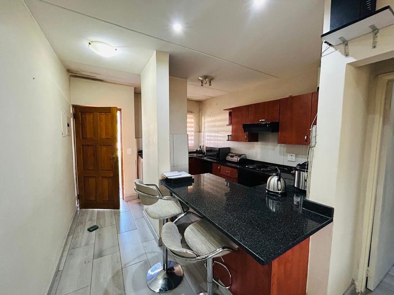 A functional kitchen featuring dark granite countertops, wooden cabinetry, and a breakfast bar, with direct access to an adjacent doorway.