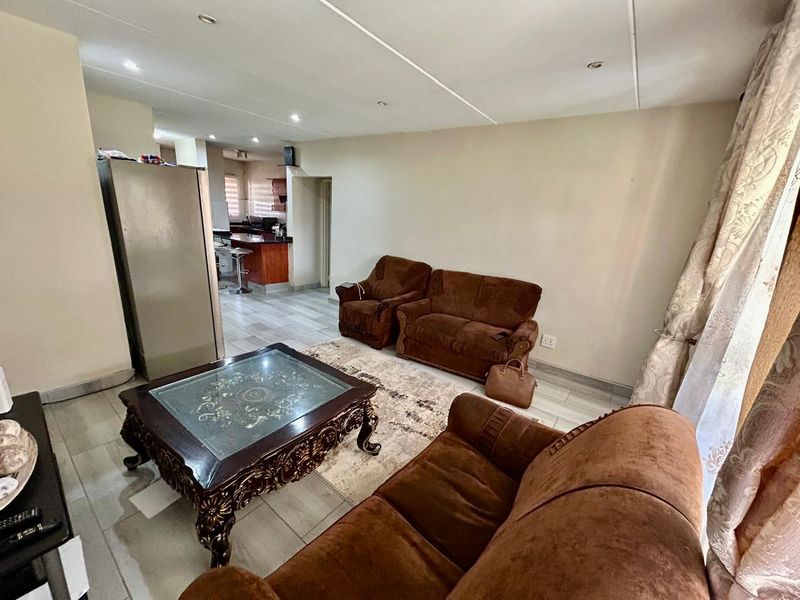 An open-plan living area featuring tiled flooring and recessed ceiling lighting, seamlessly flowing into a kitchen space with a breakfast bar.