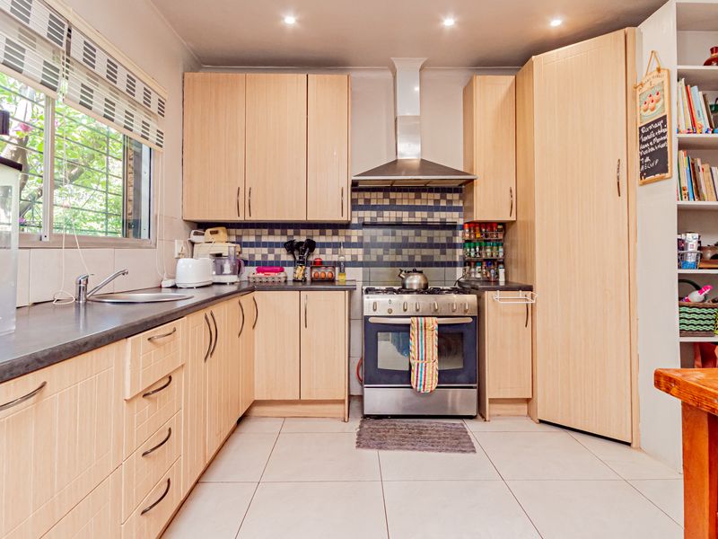 Functional kitchen featuring light wood cabinetry, stainless steel stove with extractor fan, tiled backsplash, and ample storage space.