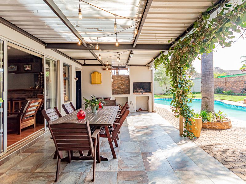Covered outdoor patio featuring a built-in braai, tiled flooring, and direct access to the swimming pool area through sliding glass doors.