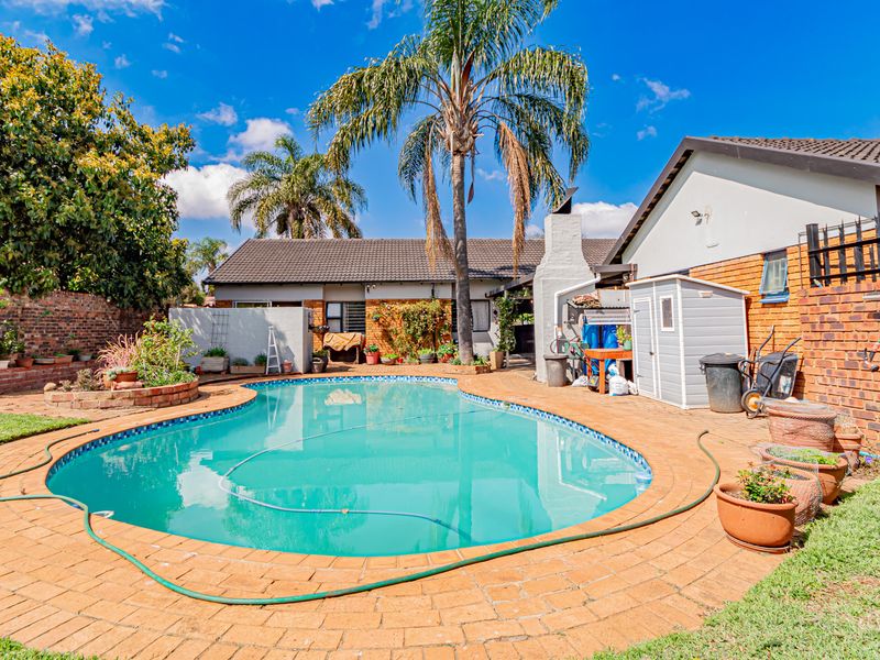 A spacious backyard featuring a swimming pool with brick paving, an outdoor fireplace, and established garden surroundings.