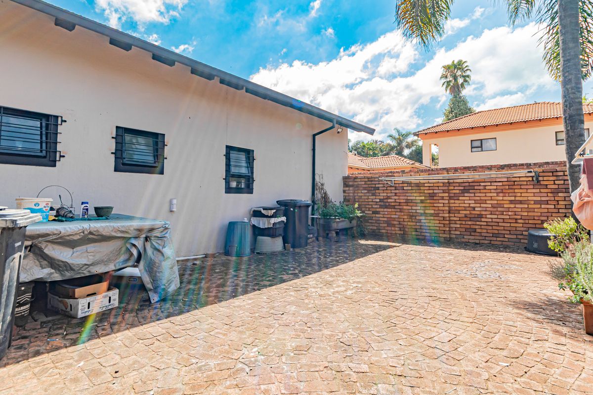 A paved rear courtyard area featuring a brick boundary wall and exterior windows with security bars.