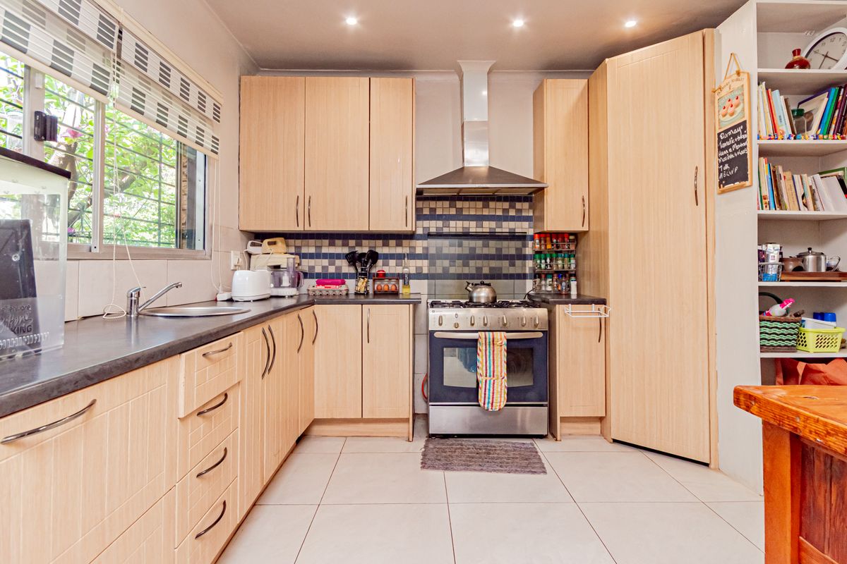 Functional kitchen featuring light wood cabinetry, stainless steel stove with extractor fan, tiled backsplash, and ample storage space.