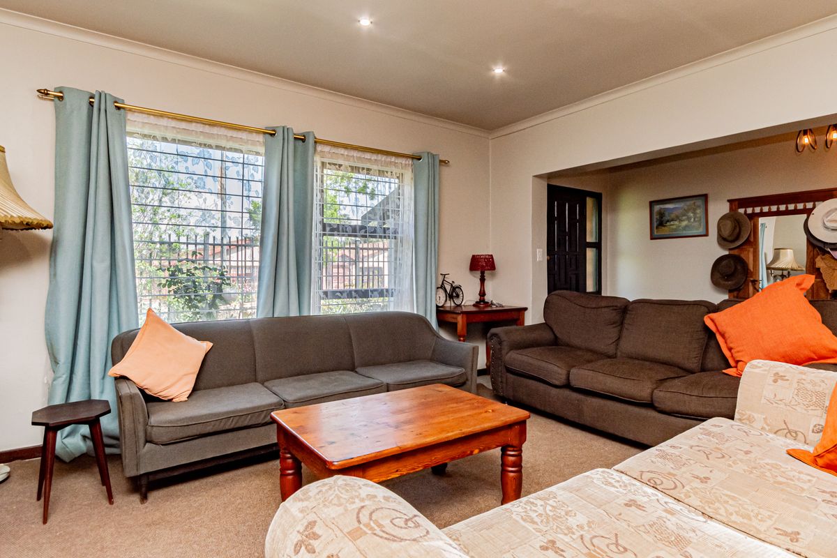 A comfortable living room featuring recessed downlighting, coving, and large windows fitted with security bars, offering a functional and well-lit space.