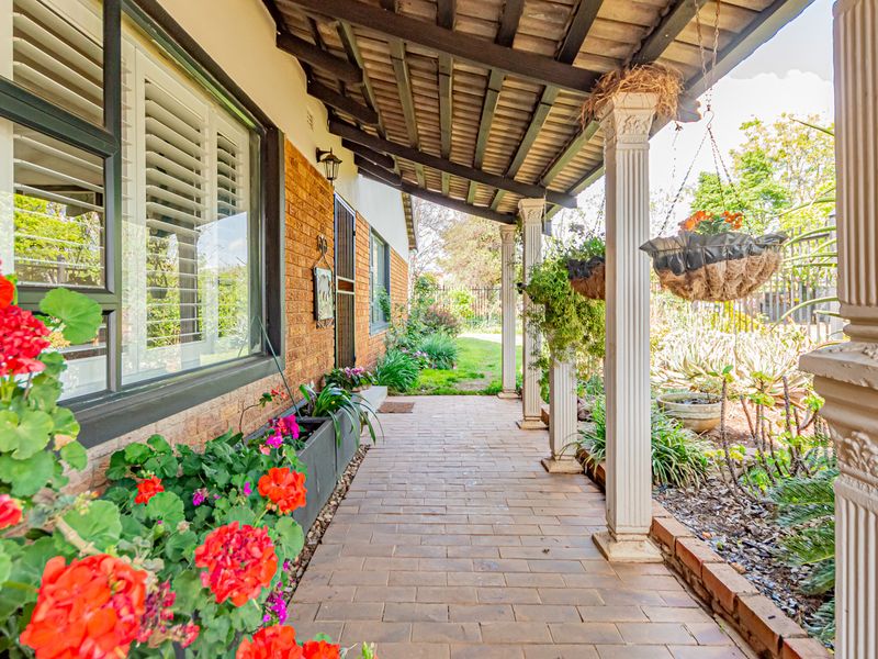 A covered patio area featuring brick paving, decorative columns, and exposed timber rafters, overlooking a landscaped garden.
