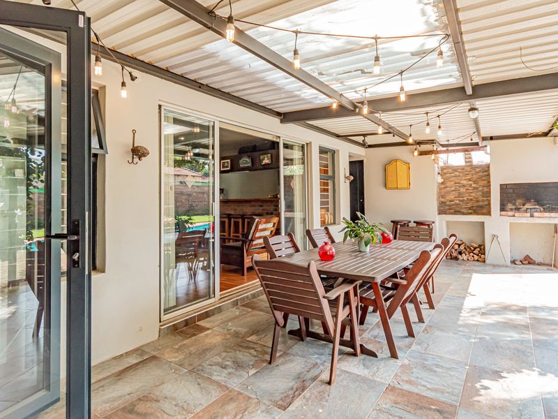 Spacious covered patio featuring tiled flooring, a built-in braai with stone cladding, and direct access to the interior through large sliding glass doors.