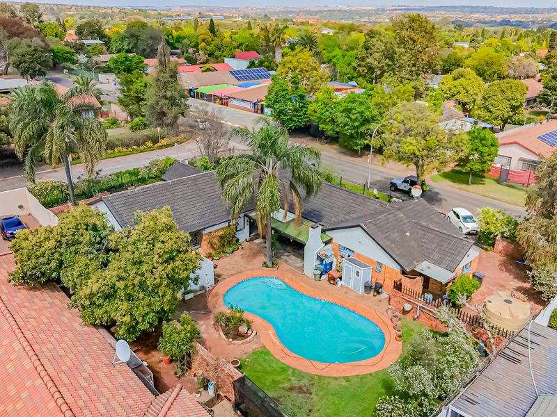 Aerial view of a residential property featuring a swimming pool, landscaped garden, and tiled roof structure within a suburban neighborhood setting.