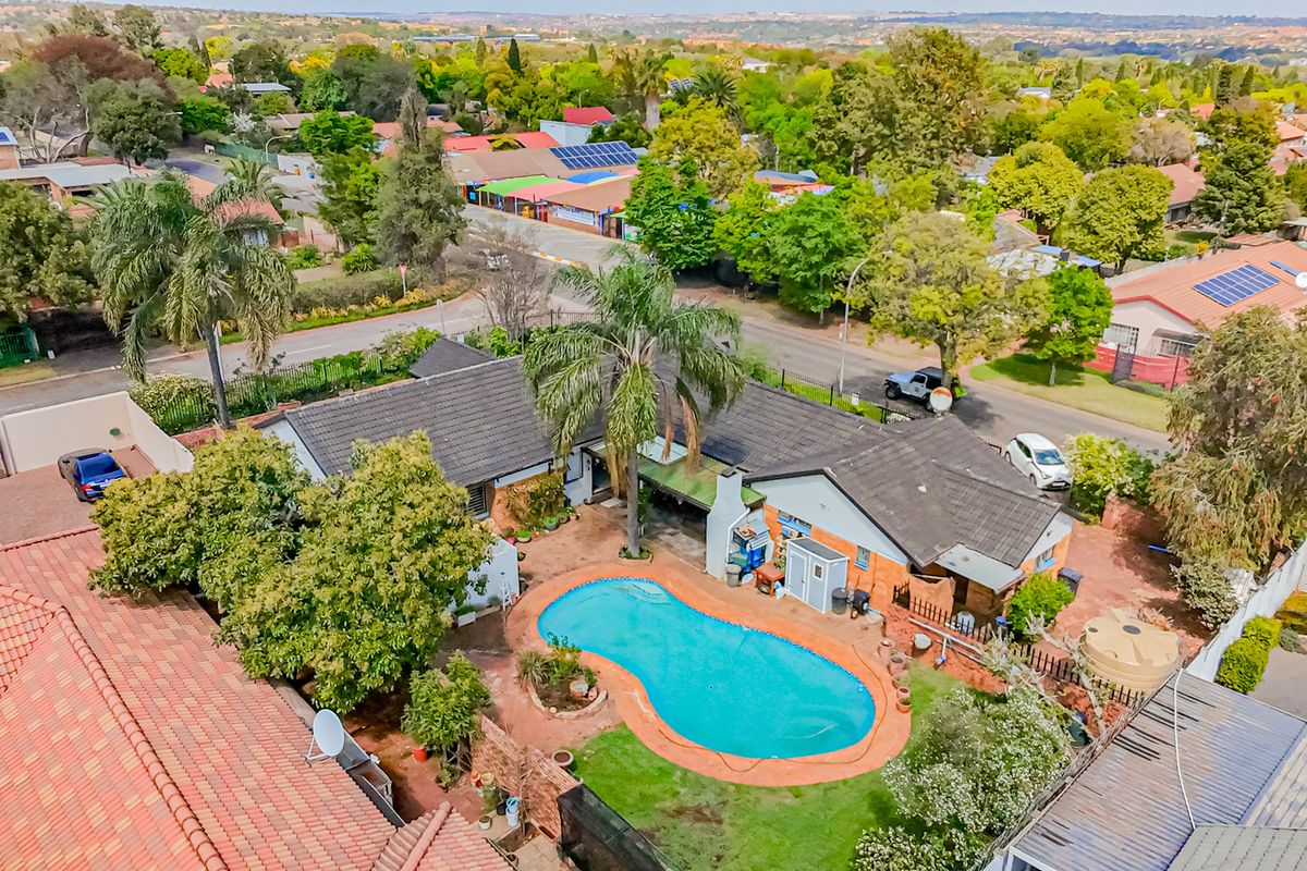 Aerial view of a residential property featuring a swimming pool, landscaped garden, and tiled roof structure within a suburban neighborhood setting.