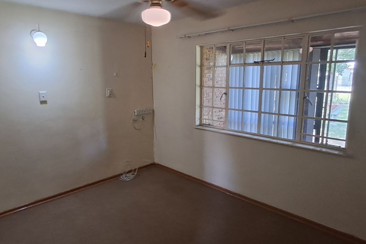 An empty bedroom featuring a ceiling fan, steel-framed window, and wall-mounted lighting, offering a blank canvas for renovation or restyling.