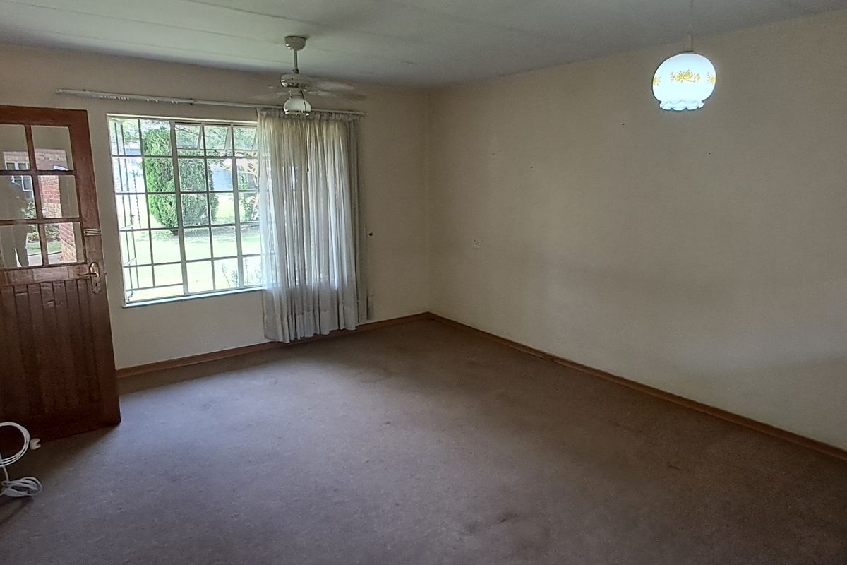 An empty living room featuring carpet flooring, a ceiling fan, and a timber-framed door leading to the exterior.