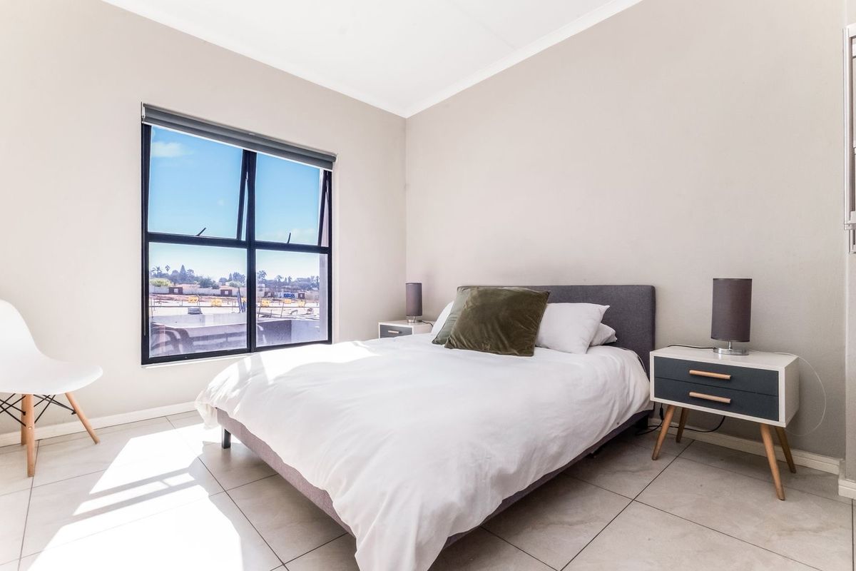 A bright and modern bedroom featuring large windows, neutral wall tones, and tiled flooring, offering a clean and comfortable living space.