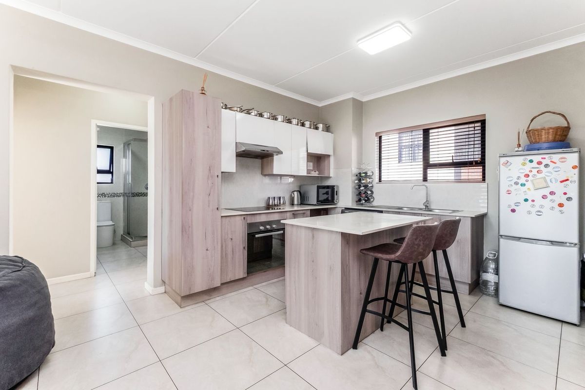 Modern kitchen featuring light wood-tone cabinetry, stone-look countertops, a central island with breakfast bar seating, and integrated stainless steel oven and extractor fan.