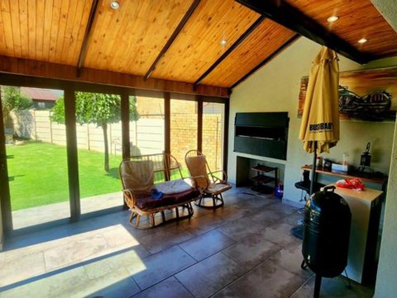 Covered patio featuring a timber-clad vaulted ceiling, tiled flooring, and a built-in braai, with sliding glass doors opening onto the garden.