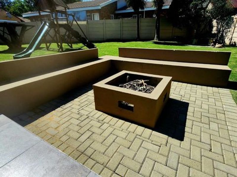 Outdoor entertainment area featuring a paved patio with built-in concrete seating and a central fire pit, set within a private garden.