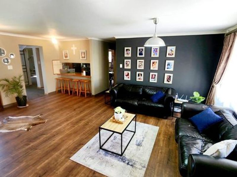 Spacious open-plan living area featuring dark wood-look laminate flooring, a breakfast bar, and a feature wall, creating a comfortable and functional family space.