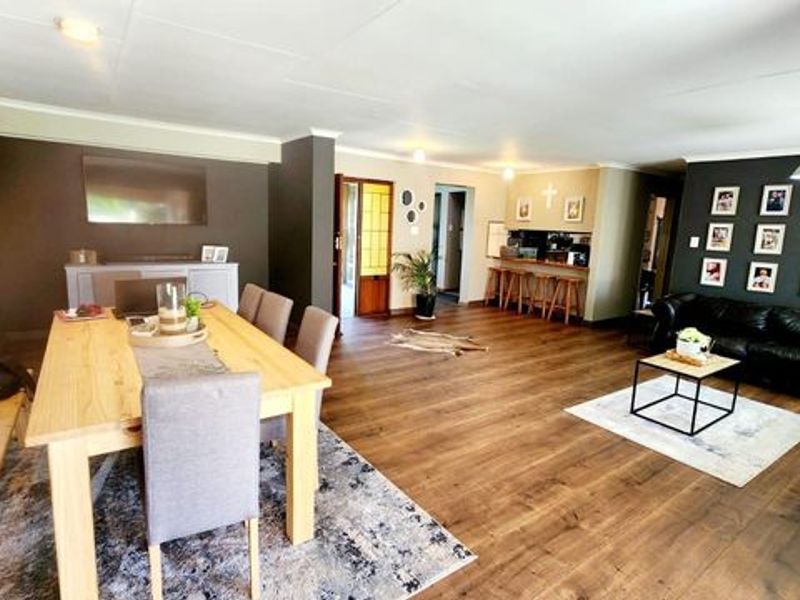 Spacious open-plan living and dining area featuring warm laminate flooring, neutral wall tones, and a convenient built-in breakfast bar.