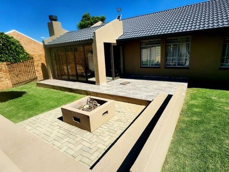 Rear exterior view featuring a tiled patio, built-in fire pit with concrete bench seating, and a well-maintained lawn area.