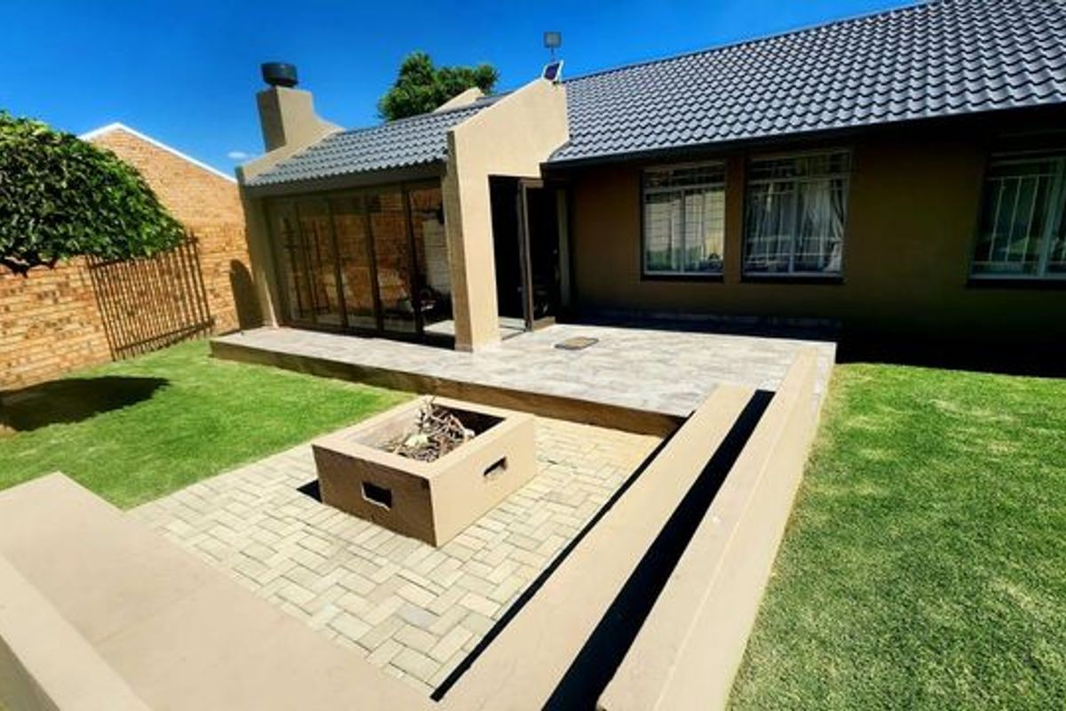 Rear exterior view featuring a tiled patio, built-in fire pit with concrete bench seating, and a well-maintained lawn area.