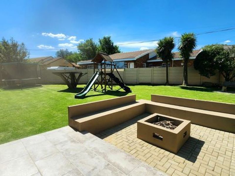 Spacious rear garden featuring a paved patio area with a built-in fire pit and concrete bench seating, surrounded by a lawn and boundary wall.